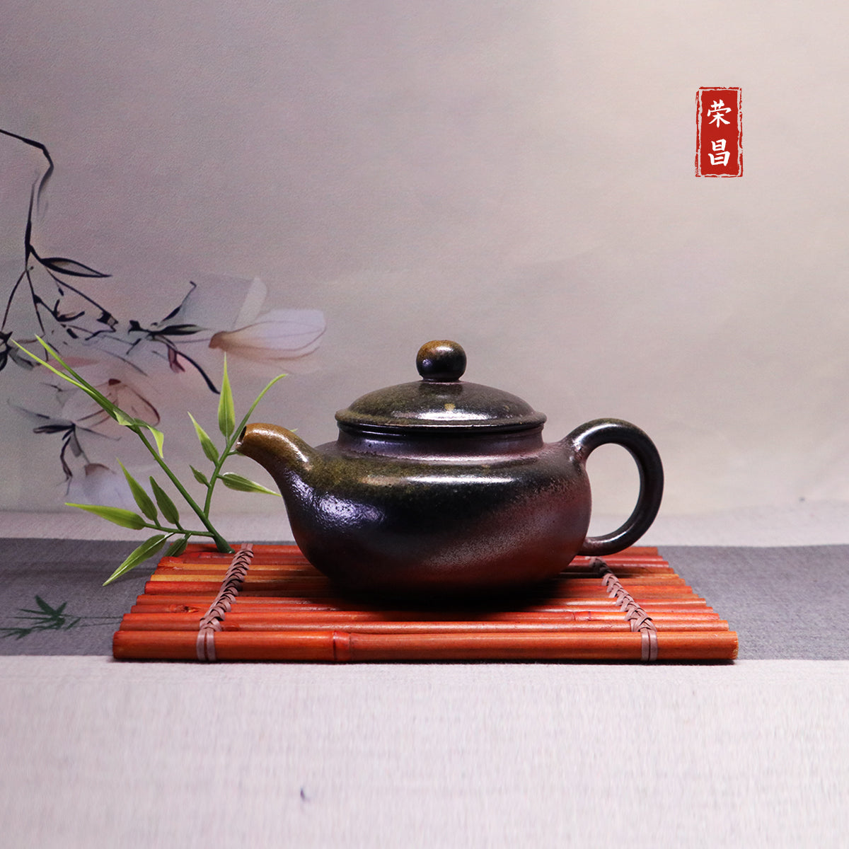 Chinese Handcrafted Fanggu Teapot in dark ceramic on bamboo mat with green leaves decoration