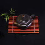 Chinese Handcrafted Fanggu Teapot made of pure handmade ceramics on a bamboo mat with green leaves
