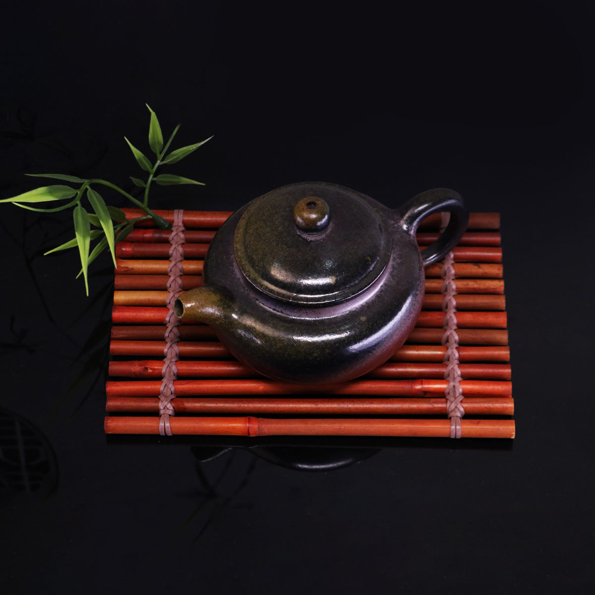 Chinese Handcrafted Fanggu Teapot made of pure handmade ceramics on a bamboo mat with green leaves