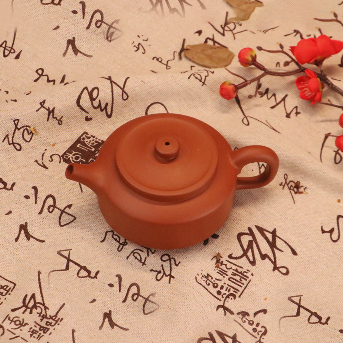 Chinese Rongchang handcrafted teapot in reddish-brown clay on calligraphy fabric with red flowers